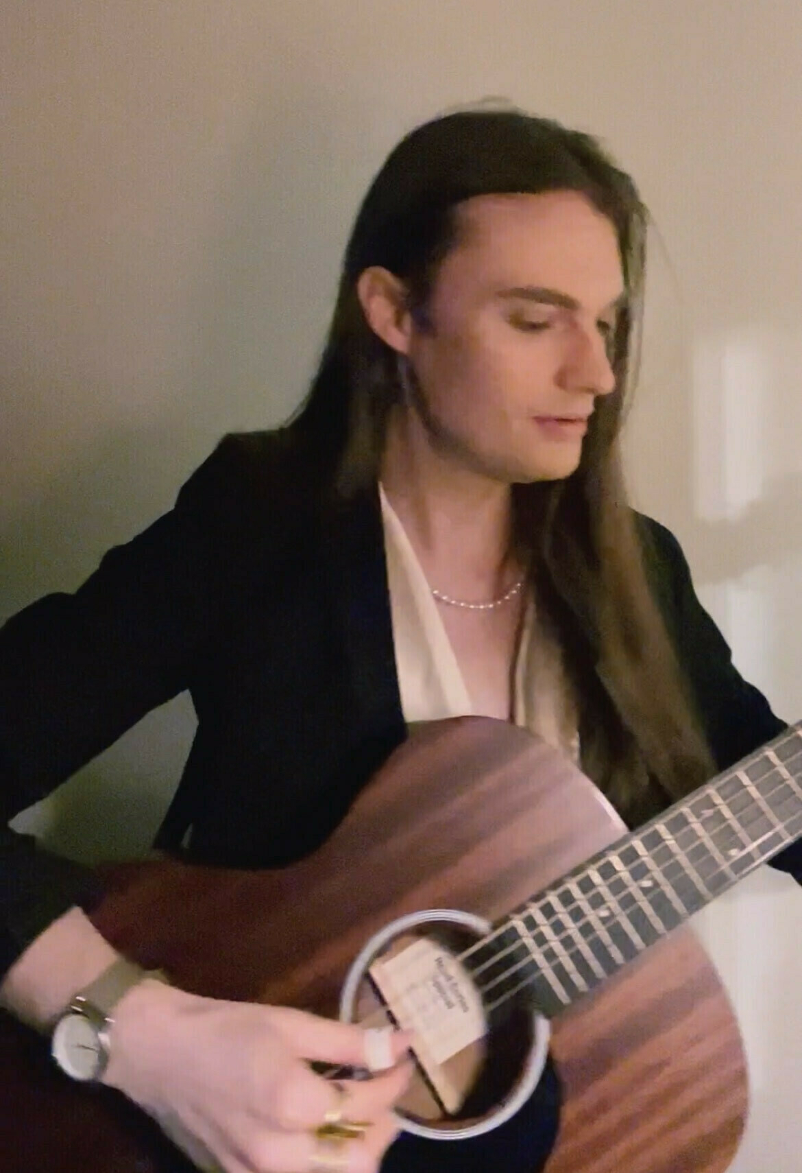 Hunter's wearing a satin shirt and black blazer. His long brown hair is down. His guitar is strapped on.