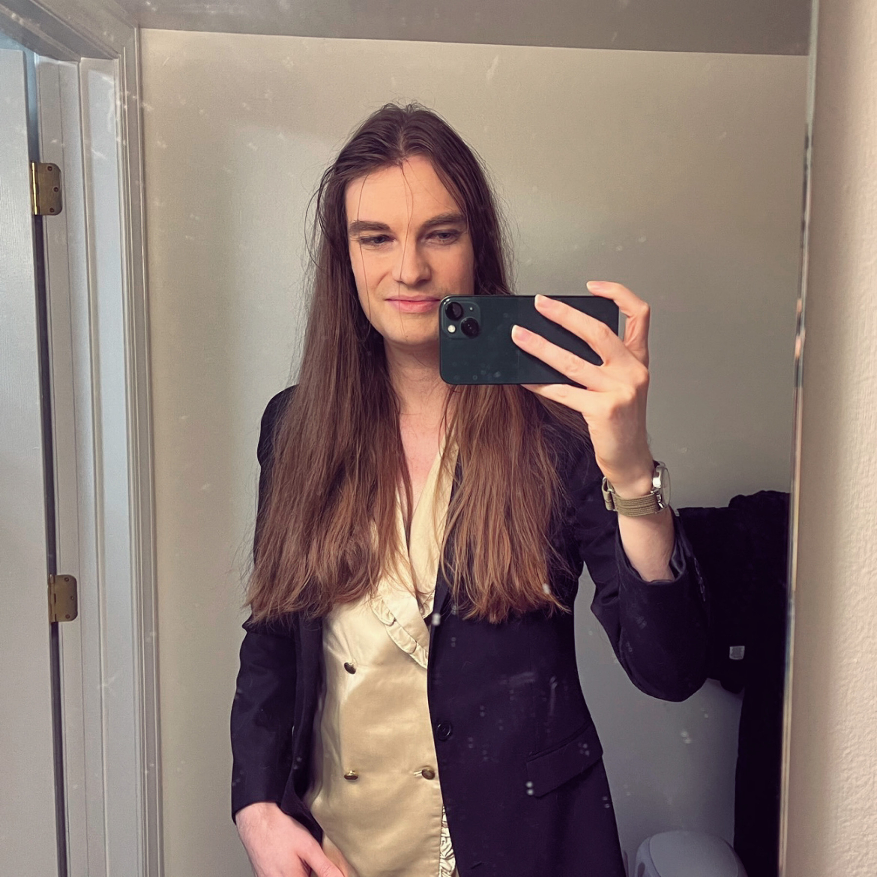 Hunter wears a champagne satin shirt and black blazer. His long brown hair is about as brushed as it ever gets. H'es a pretty pale, androgynous-looking guy.